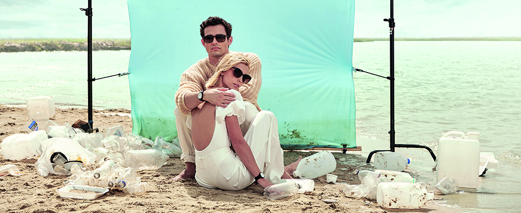Mann und Frau sitzen mit Sonnenbrillen von Sea2see an einem Plastikmüll überdeckten Strand.